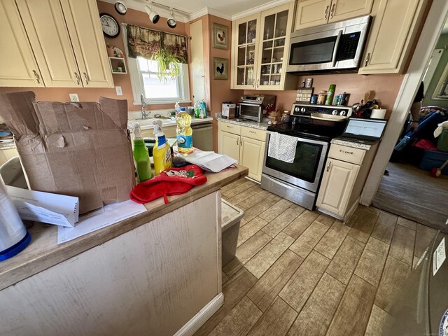 kitchen featuring glass insert cabinets, track lighting, stainless steel appliances, light wood-style flooring, and cream cabinetry