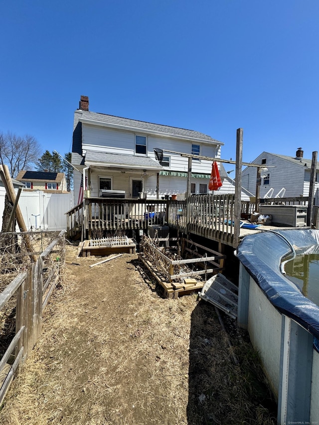 back of property with a chimney, a wooden deck, and fence