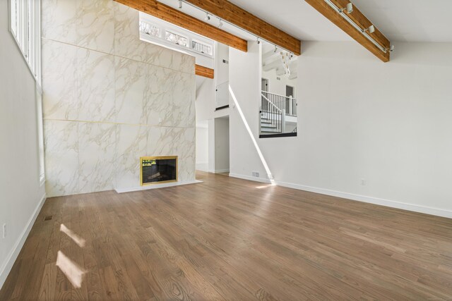 unfurnished living room featuring beamed ceiling, baseboards, wood finished floors, and stairs