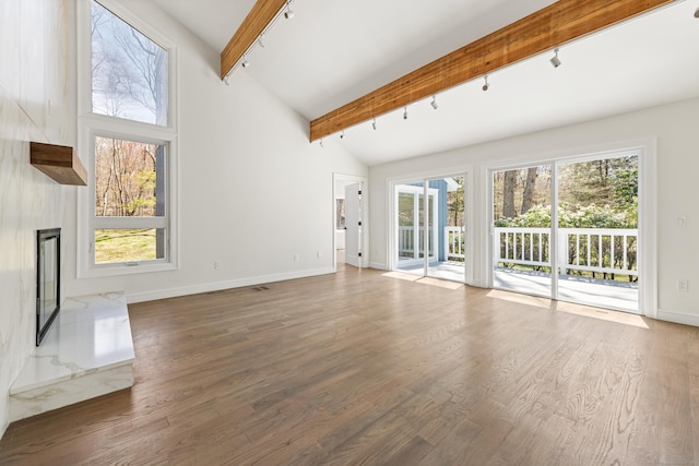 unfurnished living room with wood finished floors, rail lighting, beamed ceiling, baseboards, and high vaulted ceiling