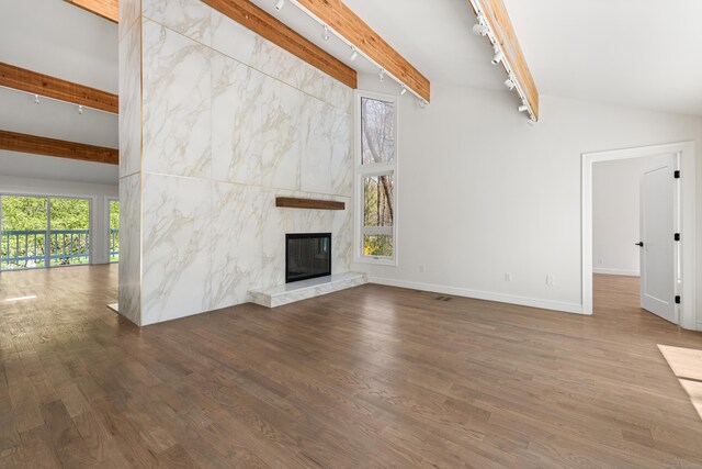 unfurnished living room featuring lofted ceiling with beams, baseboards, wood finished floors, a fireplace, and rail lighting