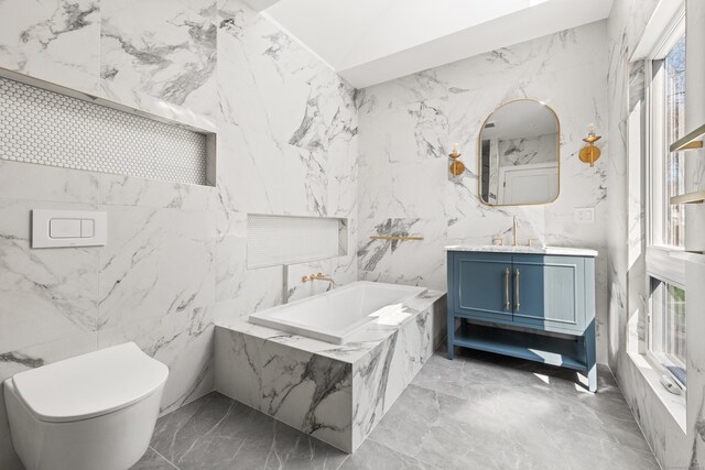 bathroom featuring a bath, toilet, stone wall, marble finish floor, and vanity