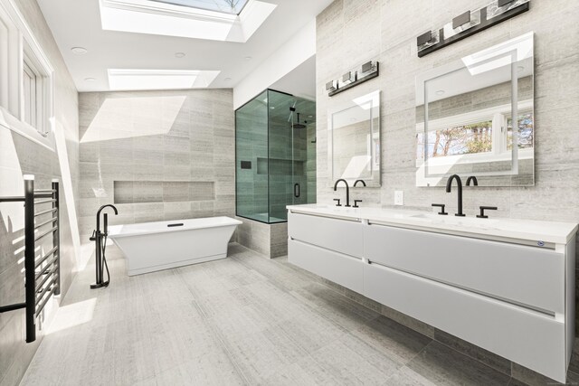 full bathroom featuring a stall shower, a skylight, tile walls, double vanity, and a freestanding bath