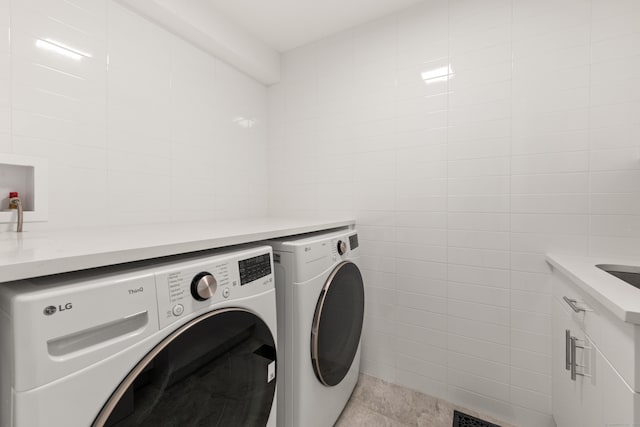 clothes washing area with tile patterned flooring, tile walls, and washing machine and clothes dryer