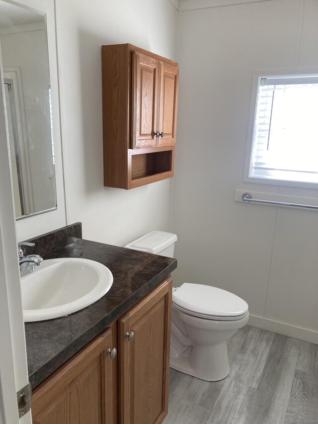 half bathroom with toilet, wood finished floors, and vanity