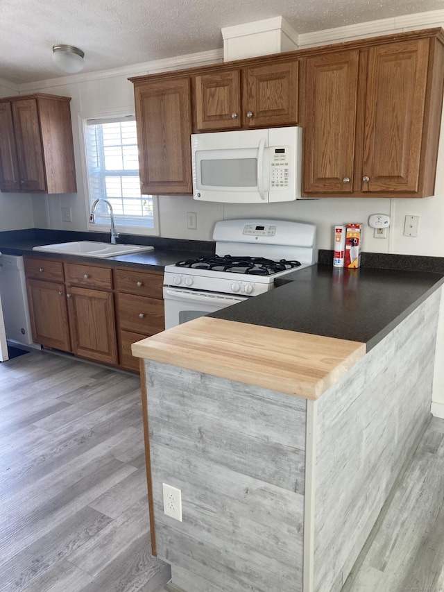 kitchen with a sink, a peninsula, brown cabinets, and white appliances