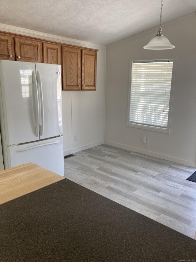 kitchen featuring freestanding refrigerator, brown cabinets, pendant lighting, and light wood-type flooring