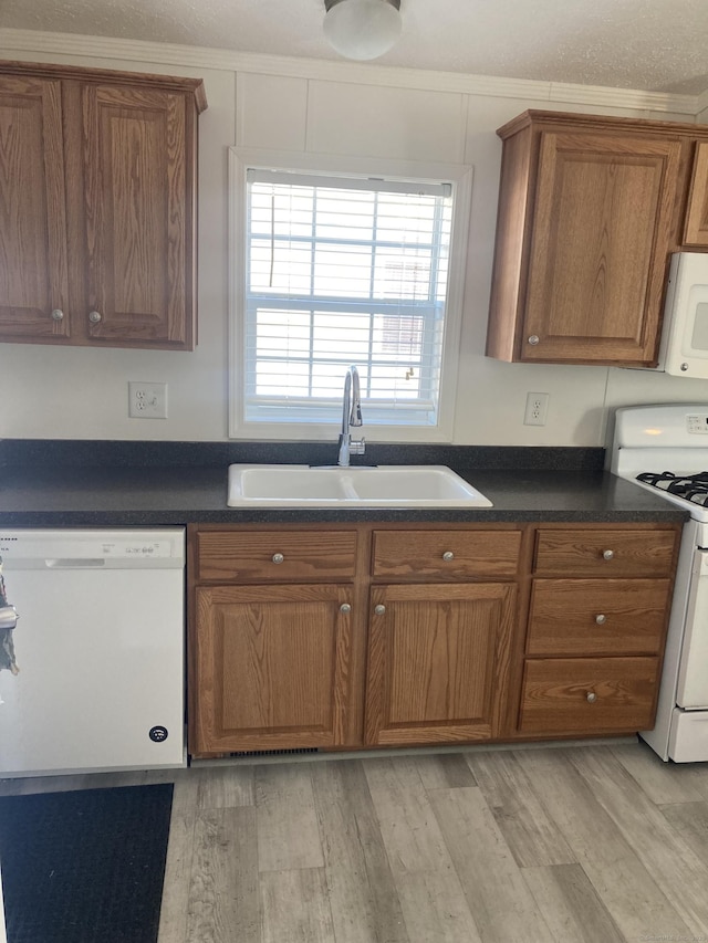 kitchen featuring white appliances, brown cabinets, dark countertops, and a sink