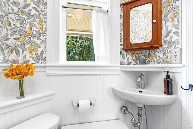 bathroom featuring a wainscoted wall, wallpapered walls, and toilet