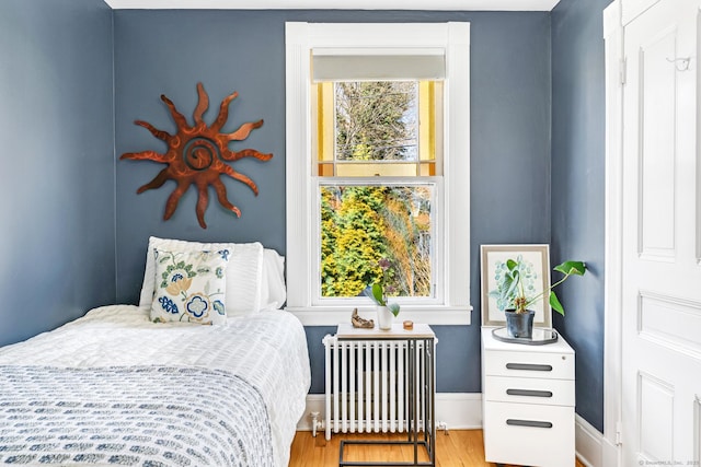 bedroom with wood finished floors, baseboards, and radiator heating unit