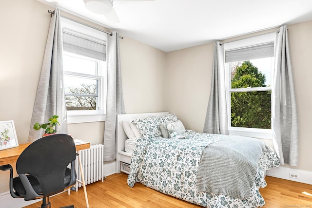 bedroom featuring wood finished floors, baseboards, radiator heating unit, and multiple windows