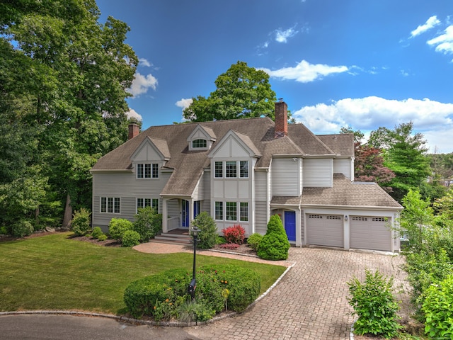 view of front of home with a chimney, an attached garage, decorative driveway, and a front lawn