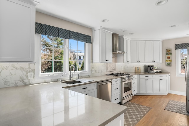 kitchen with wall chimney range hood, stainless steel appliances, a sink, and backsplash