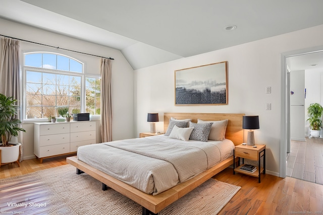 bedroom with baseboards, vaulted ceiling, and light wood finished floors