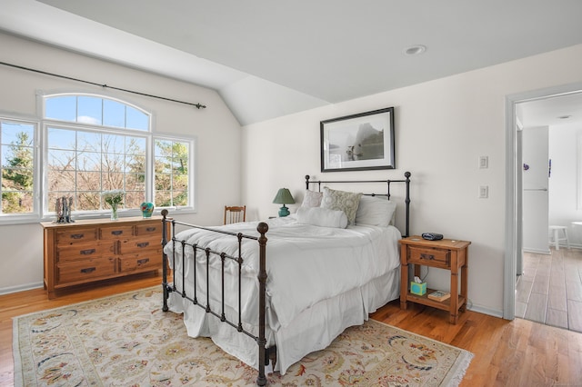 bedroom featuring baseboards, lofted ceiling, and light wood finished floors