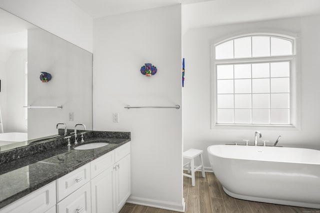 bathroom featuring a freestanding tub, vanity, baseboards, and wood finished floors