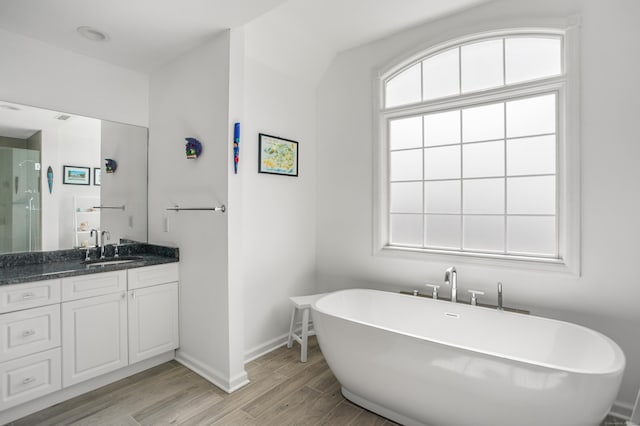 bathroom featuring a stall shower, wood finished floors, baseboards, vanity, and a soaking tub
