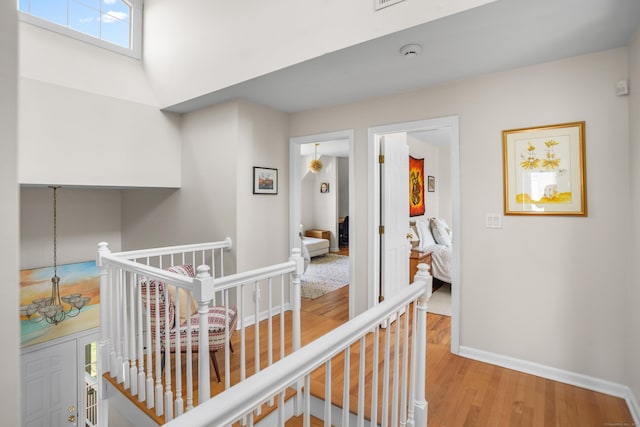 corridor featuring baseboards, an upstairs landing, and wood finished floors