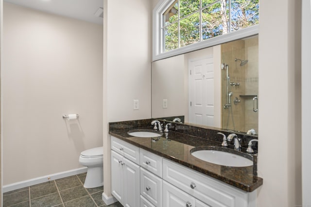 bathroom featuring toilet, baseboards, tiled shower, and a sink