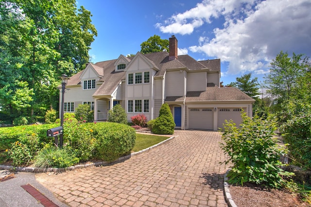 view of front of home with an attached garage, driveway, a chimney, and a shingled roof