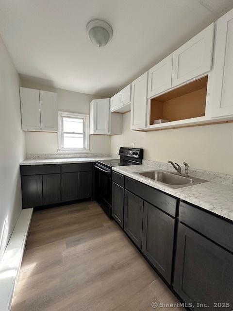 kitchen featuring light wood finished floors, black electric range, a sink, and white cabinetry