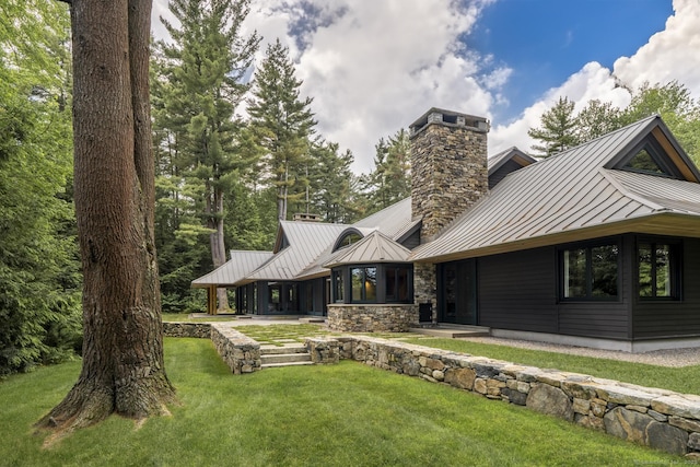 back of house featuring stone siding, a standing seam roof, a yard, and metal roof