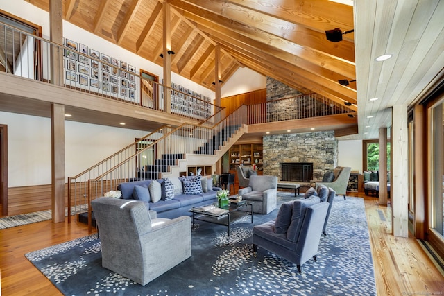 living area featuring wood finished floors, stairway, wooden ceiling, a stone fireplace, and high vaulted ceiling