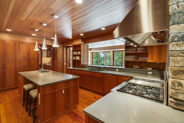 kitchen featuring open shelves, a sink, brown cabinets, a kitchen island with sink, and wall chimney exhaust hood