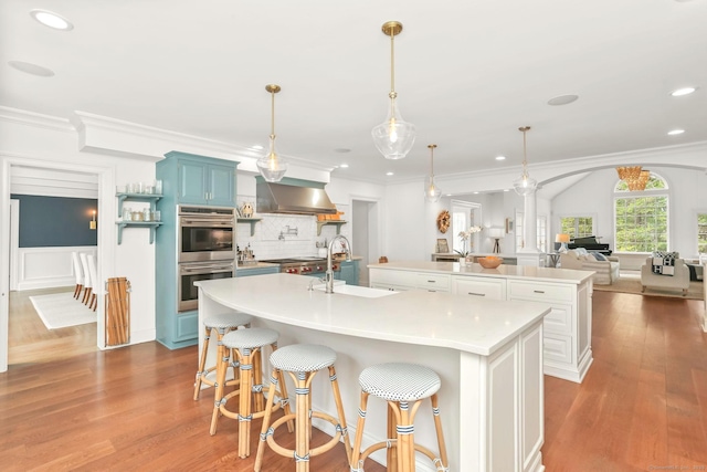 47 Peaceable St, Ridgefield, CT 06877 - kitchen featuring a sink, a large island with sink, double oven, blue cabinets, and wall chimney exhaust hood