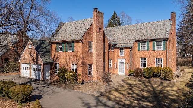 view of front of home featuring a garage, driveway, a chimney, and brick siding