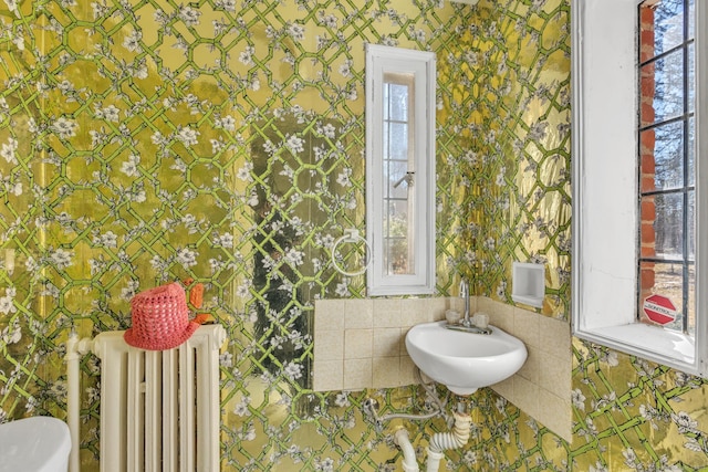 bathroom with radiator, wallpapered walls, and a sink