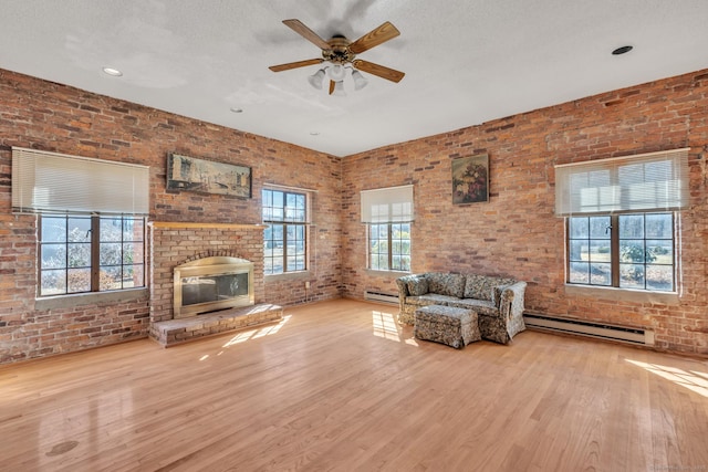 unfurnished living room with baseboard heating, brick wall, a ceiling fan, and wood finished floors