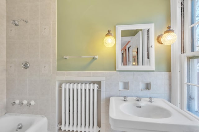 bathroom featuring washtub / shower combination, radiator heating unit, tile walls, and a sink