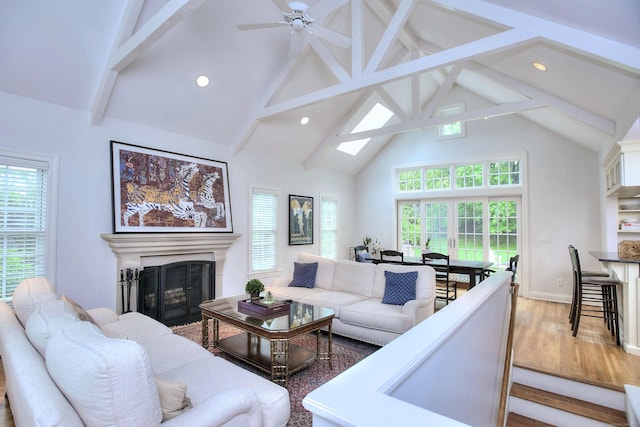living area with wood finished floors, a fireplace, beamed ceiling, and high vaulted ceiling