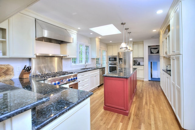 kitchen featuring recessed lighting, light wood finished floors, wall chimney exhaust hood, appliances with stainless steel finishes, and a skylight