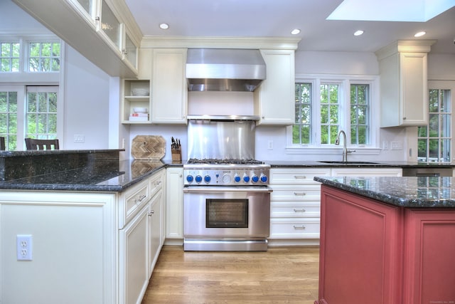 kitchen featuring a sink, a skylight, light wood-type flooring, wall chimney exhaust hood, and stainless steel stove