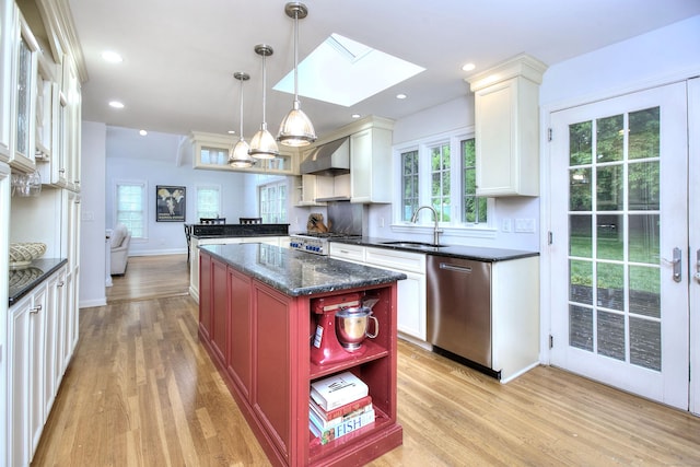 kitchen with stainless steel dishwasher, light wood-style flooring, a skylight, and a sink