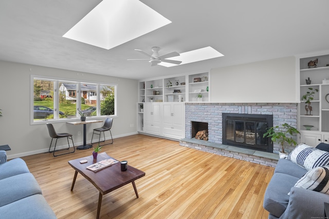 living area with a skylight, ceiling fan, a brick fireplace, and wood finished floors
