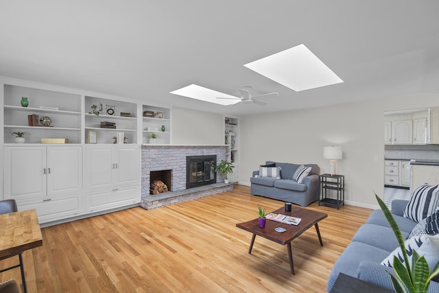 living room featuring light wood finished floors, a brick fireplace, built in features, baseboards, and a skylight