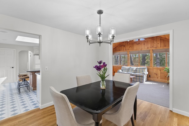 dining area featuring baseboards, arched walkways, light wood-style flooring, and a notable chandelier