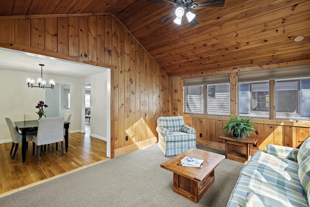 living room featuring wooden walls, ceiling fan with notable chandelier, vaulted ceiling, and wooden ceiling