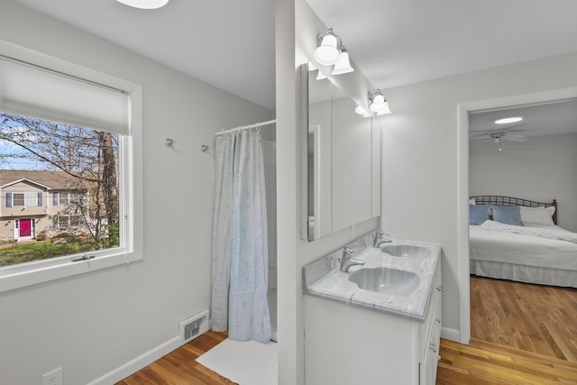 ensuite bathroom with a sink, curtained shower, ensuite bathroom, wood finished floors, and visible vents