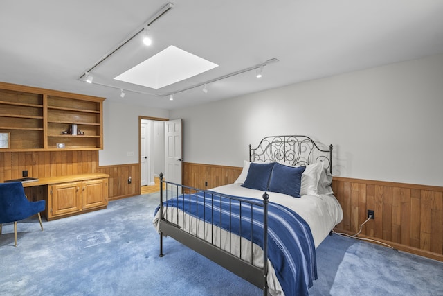 bedroom with wainscoting, wooden walls, built in desk, rail lighting, and a skylight