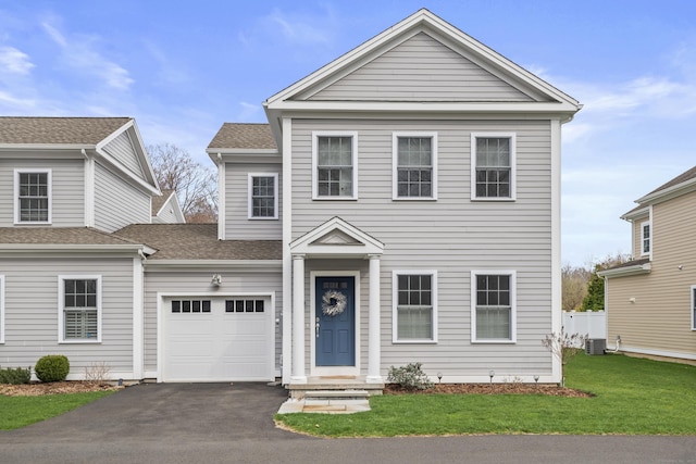 traditional-style home with a garage, a front lawn, central AC, a shingled roof, and driveway