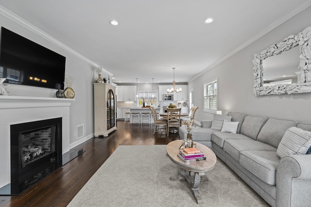 living area featuring crown molding, a notable chandelier, dark wood finished floors, a glass covered fireplace, and baseboards