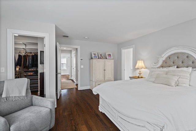 bedroom featuring a walk in closet, baseboards, visible vents, dark wood-style floors, and a closet