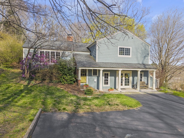 view of front of property featuring a chimney, roof with shingles, a porch, and a front yard
