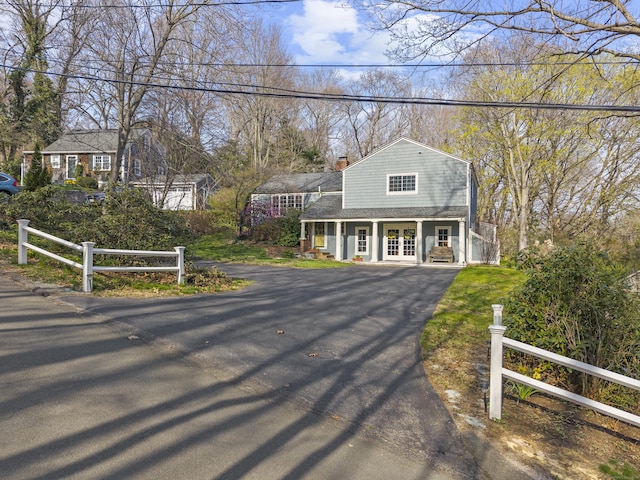 view of front of home with a gambrel roof, aphalt driveway, fence, french doors, and a porch