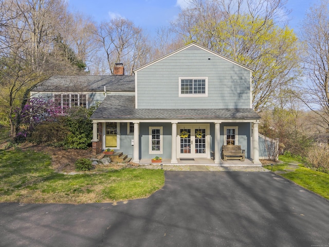 view of front of house featuring french doors, roof with shingles, a chimney, and covered porch