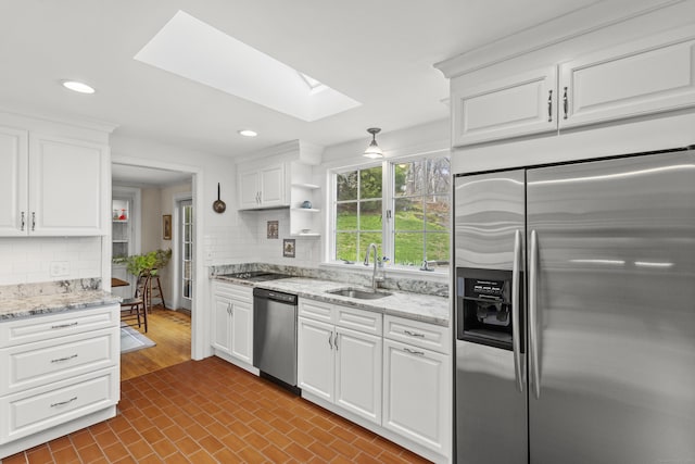 kitchen with backsplash, appliances with stainless steel finishes, a skylight, and a sink